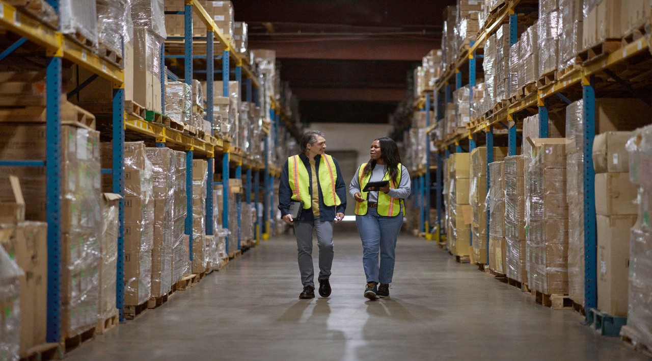 Warehouse workers walking through the aisle; manager reviewing and sharing data real time