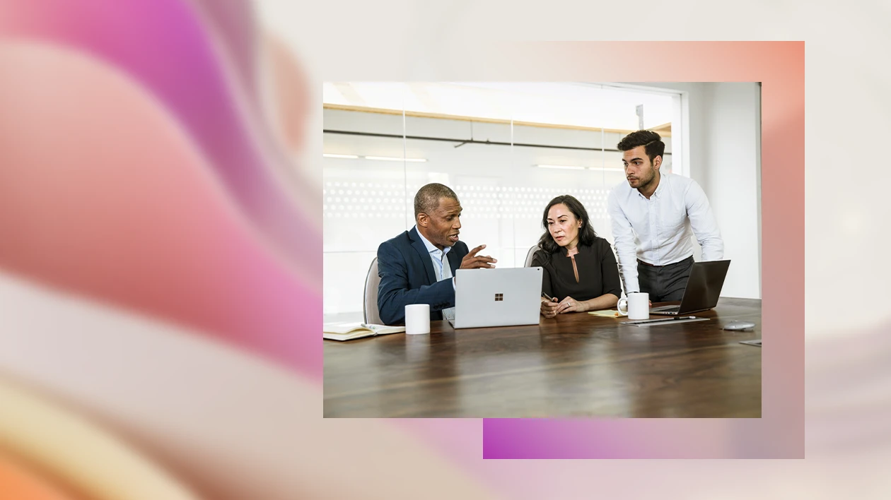 Two male and one female corporate office workers sitting at conference room table in discussion. There are two open laptops on the table.